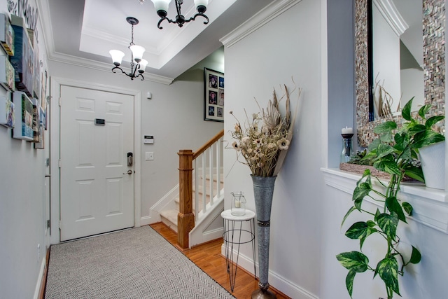 foyer entrance featuring ornamental molding, stairs, a tray ceiling, light wood-type flooring, and a notable chandelier