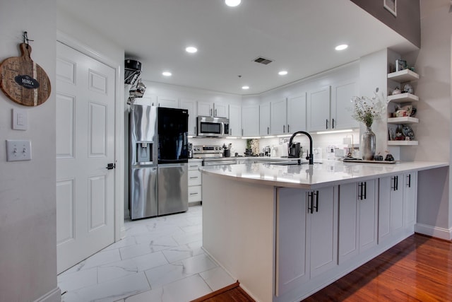 kitchen with a peninsula, a sink, visible vents, appliances with stainless steel finishes, and open shelves