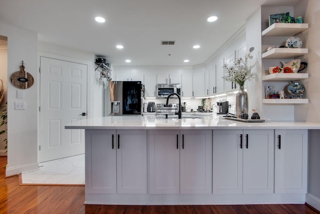 kitchen featuring a peninsula, stainless steel appliances, white cabinetry, open shelves, and a sink