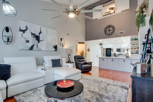 living room featuring a barn door, a ceiling fan, visible vents, and light wood-style floors