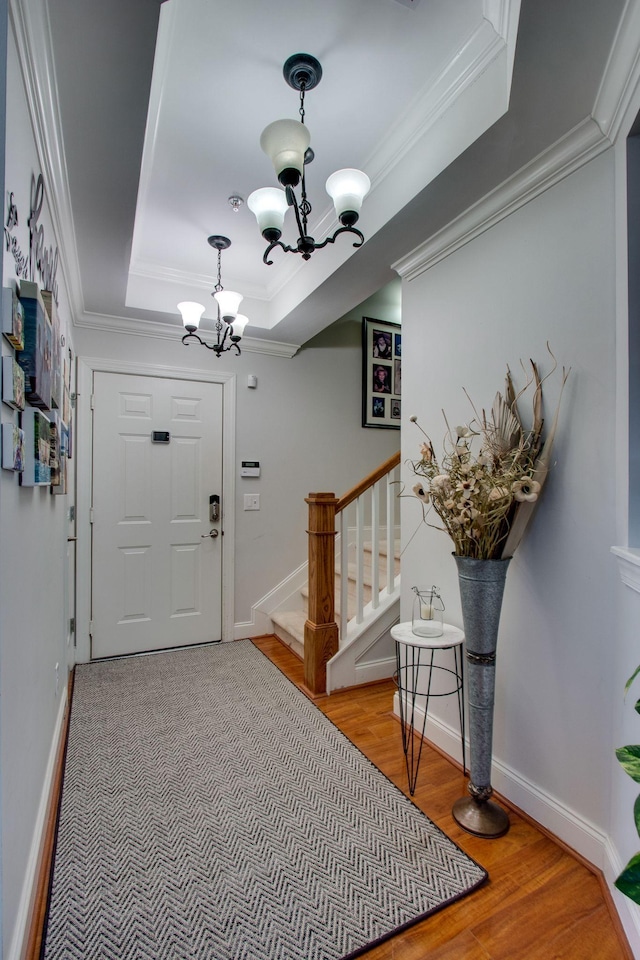 entryway featuring a notable chandelier, a raised ceiling, stairway, ornamental molding, and wood finished floors