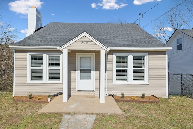 bungalow-style house with a shingled roof, a front yard, fence, and a chimney