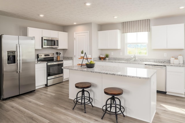 kitchen featuring a breakfast bar, light wood-style flooring, appliances with stainless steel finishes, white cabinets, and a kitchen island