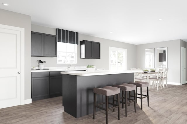 kitchen with a center island, light wood finished floors, a kitchen bar, light countertops, and baseboards