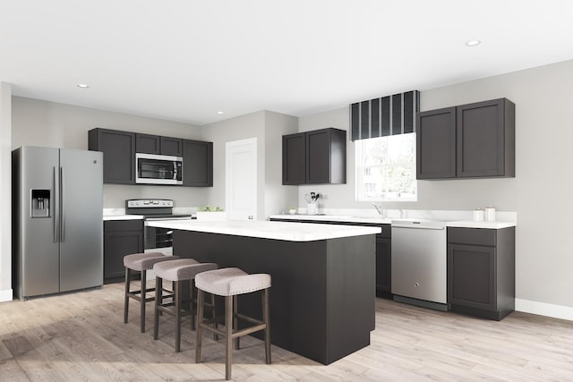 kitchen featuring a center island, light wood finished floors, light countertops, appliances with stainless steel finishes, and a kitchen breakfast bar