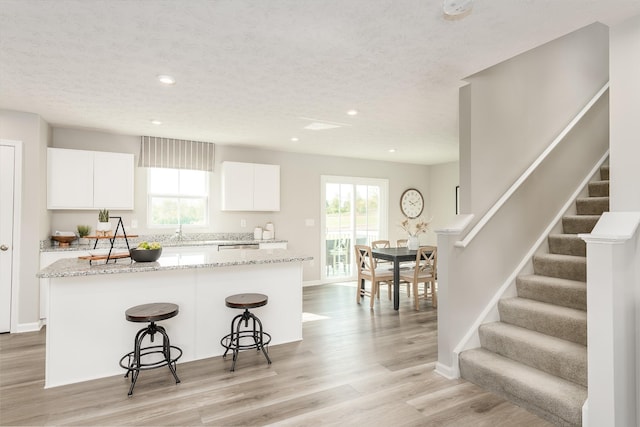 kitchen with light wood-type flooring, plenty of natural light, white cabinetry, and a breakfast bar