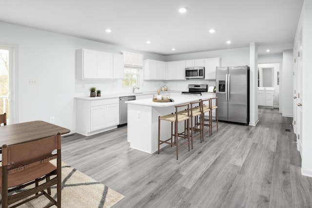 kitchen featuring a breakfast bar area, light wood-style flooring, stainless steel appliances, a kitchen island, and white cabinets