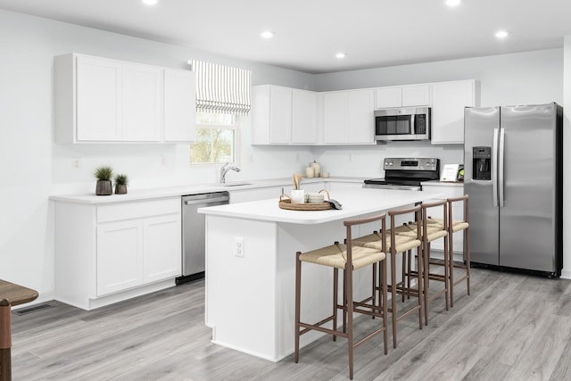 kitchen featuring stainless steel appliances, a breakfast bar, a sink, a kitchen island, and white cabinetry