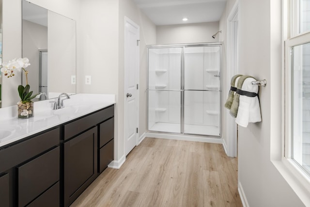 full bath with double vanity, a stall shower, a sink, and wood finished floors