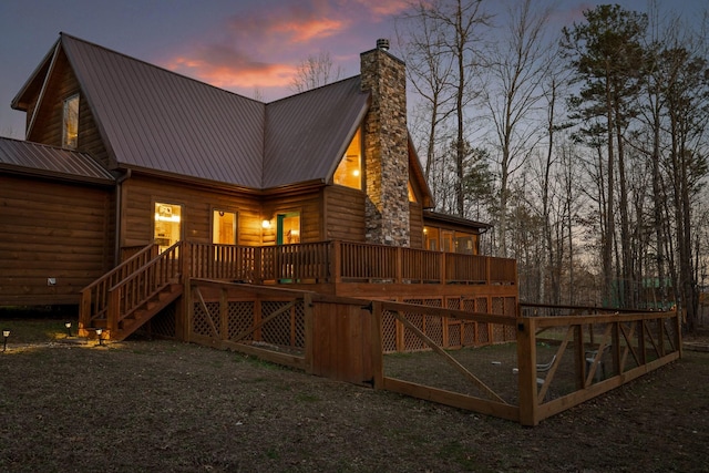 back of house with faux log siding, a chimney, stairway, metal roof, and a wooden deck