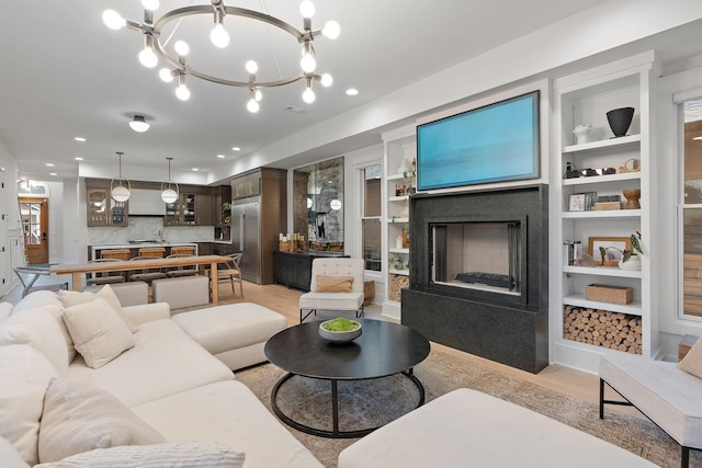 living area featuring built in shelves, recessed lighting, a fireplace with raised hearth, and a notable chandelier