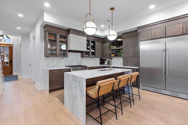 kitchen with range, light wood-type flooring, open shelves, a sink, and built in fridge