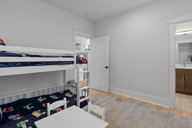 bedroom with light wood-type flooring, a sink, connected bathroom, and baseboards