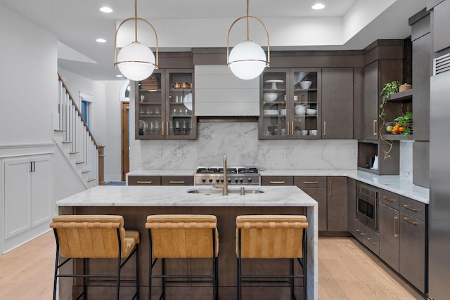 kitchen with stainless steel microwave, dark brown cabinets, light wood-style floors, open shelves, and a sink