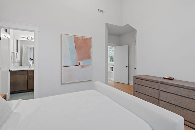 bedroom featuring light wood-style floors, visible vents, and connected bathroom