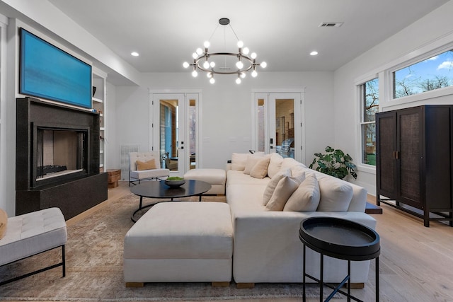 living room with a fireplace with raised hearth, french doors, wood finished floors, and visible vents