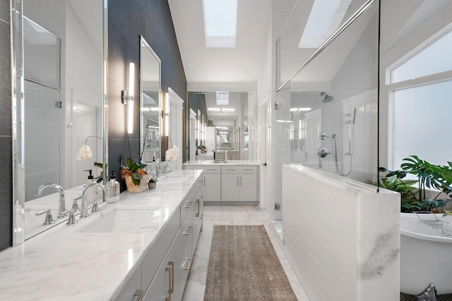 full bath featuring a skylight, two vanities, a sink, marble finish floor, and a stall shower