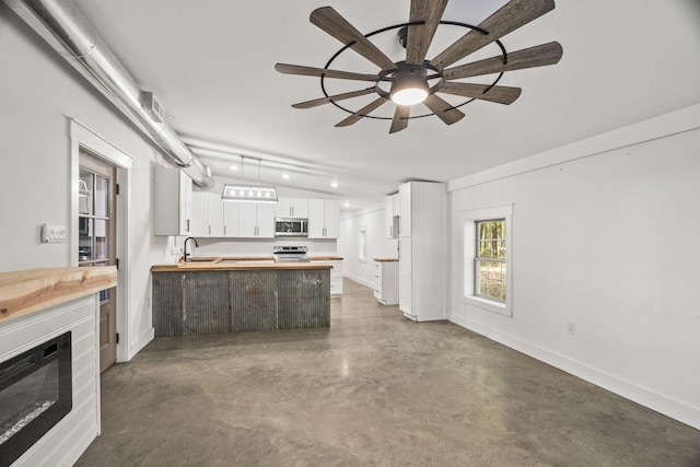 kitchen featuring finished concrete flooring, stainless steel appliances, a glass covered fireplace, white cabinets, and a sink