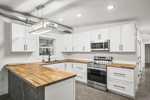 kitchen with butcher block countertops, a peninsula, stainless steel appliances, white cabinetry, and a sink