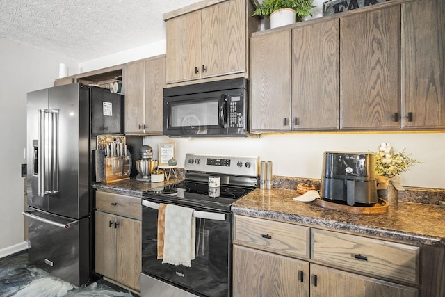 kitchen featuring baseboards, appliances with stainless steel finishes, dark stone counters, and a textured ceiling