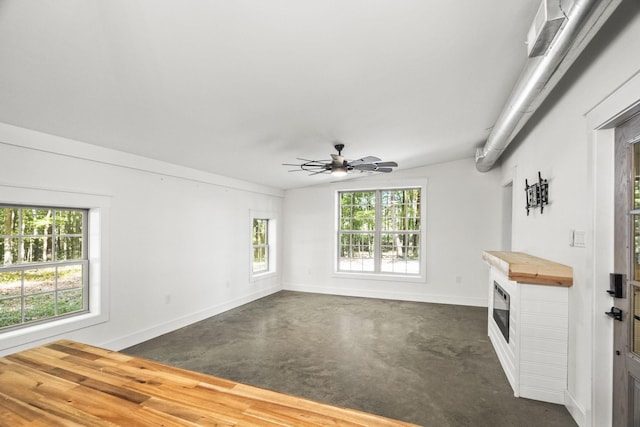 empty room with finished concrete flooring, ceiling fan, a fireplace, and baseboards