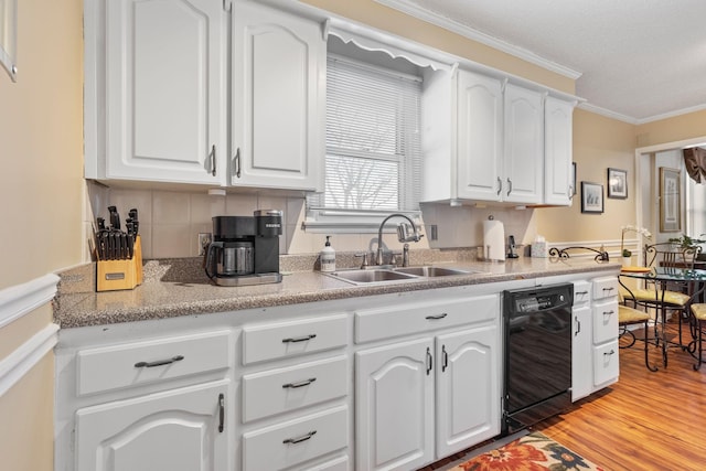 kitchen featuring black dishwasher, crown molding, light wood finished floors, white cabinetry, and a sink