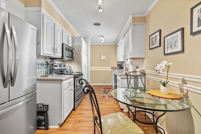 kitchen featuring crown molding, stainless steel appliances, tasteful backsplash, visible vents, and light wood-style floors