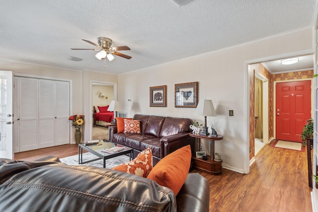 living area with baseboards, visible vents, wood finished floors, crown molding, and a textured ceiling