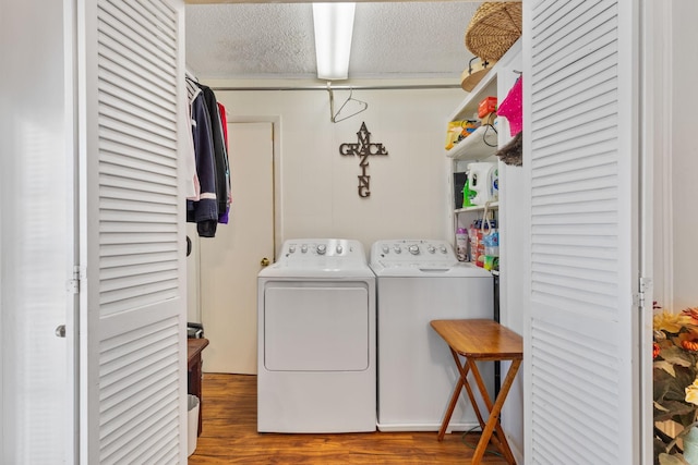 clothes washing area with washer and dryer, laundry area, a textured ceiling, and wood finished floors