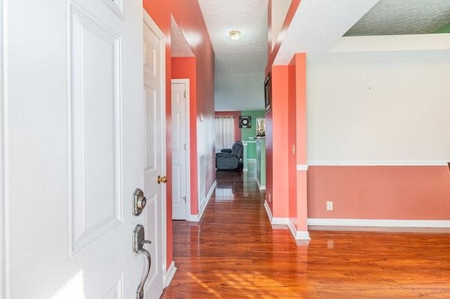 hall with wood finished floors, baseboards, and a textured ceiling