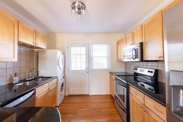 kitchen with light wood-style flooring, a sink, appliances with stainless steel finishes, dark countertops, and stacked washer and clothes dryer