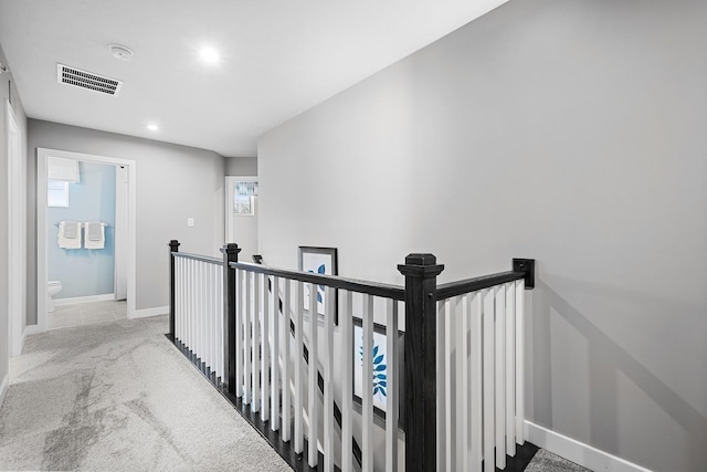 hallway with a wealth of natural light, visible vents, carpet flooring, an upstairs landing, and baseboards