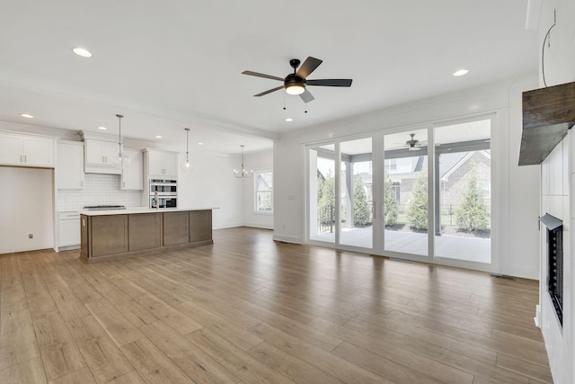 unfurnished living room featuring light wood-style flooring, recessed lighting, ceiling fan with notable chandelier, a fireplace, and baseboards