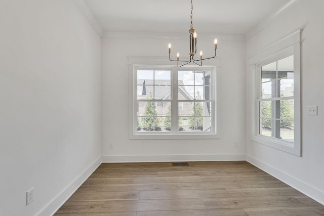 unfurnished dining area featuring ornamental molding, baseboards, an inviting chandelier, and wood finished floors