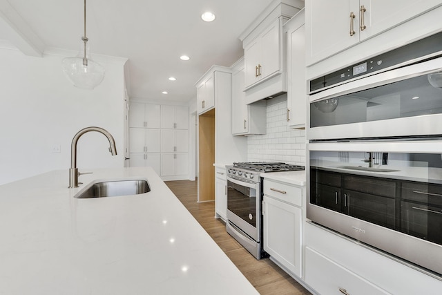 kitchen featuring light wood-style flooring, a sink, light countertops, appliances with stainless steel finishes, and backsplash