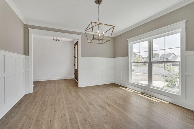 unfurnished dining area featuring a wainscoted wall, a decorative wall, light wood-style floors, ornamental molding, and a chandelier