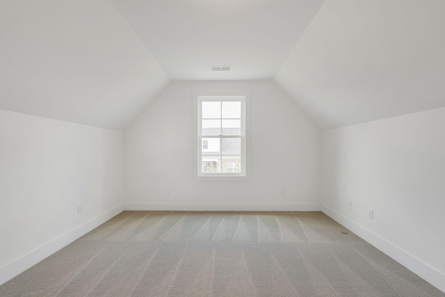 additional living space featuring lofted ceiling, baseboards, visible vents, and light colored carpet