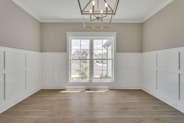 unfurnished dining area featuring light wood-style flooring, a chandelier, a decorative wall, and crown molding