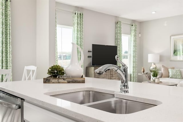 kitchen with light stone countertops, stainless steel dishwasher, open floor plan, and a sink