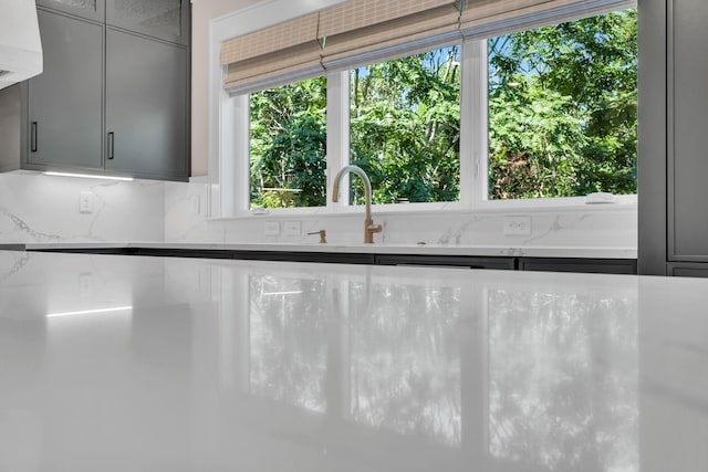 room details with a sink, backsplash, gray cabinets, and light stone countertops