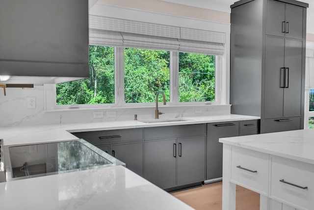 kitchen with a wealth of natural light, a sink, gray cabinetry, and light stone countertops