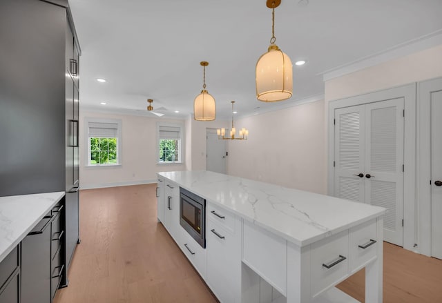 kitchen featuring built in microwave, hanging light fixtures, a center island, light wood finished floors, and crown molding