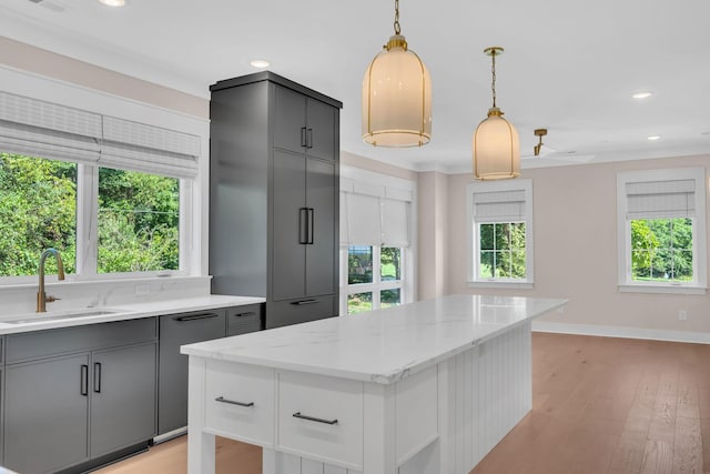 kitchen with gray cabinetry, a sink, a center island, light wood finished floors, and decorative light fixtures