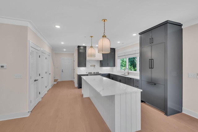 kitchen featuring light stone countertops, a kitchen island, light wood-style flooring, and crown molding