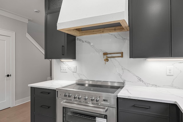 kitchen with range hood, gray cabinets, backsplash, and stainless steel stove