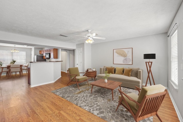 living room featuring light wood-type flooring, plenty of natural light, visible vents, and a textured ceiling