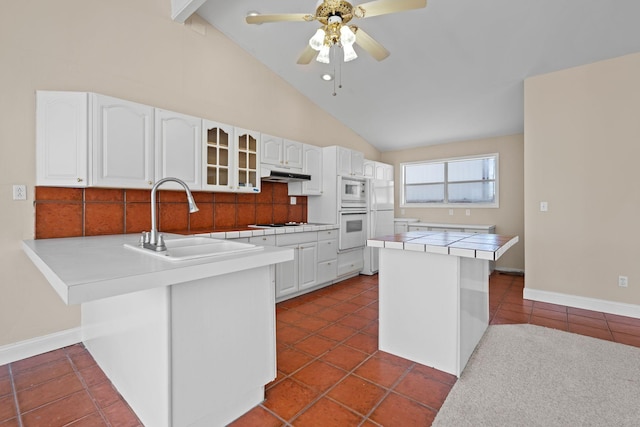 kitchen with glass insert cabinets, white cabinets, a sink, white appliances, and a peninsula