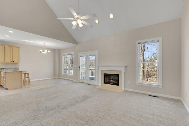 unfurnished living room with ceiling fan with notable chandelier, baseboards, a fireplace with flush hearth, and light colored carpet