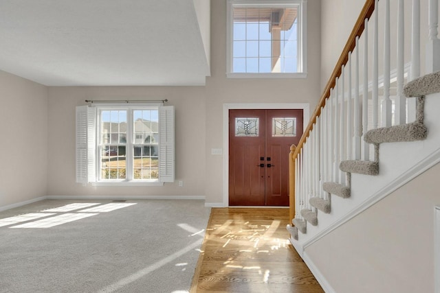 carpeted entrance foyer featuring stairs, a high ceiling, and baseboards