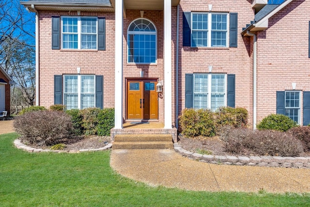 view of exterior entry featuring brick siding and a lawn